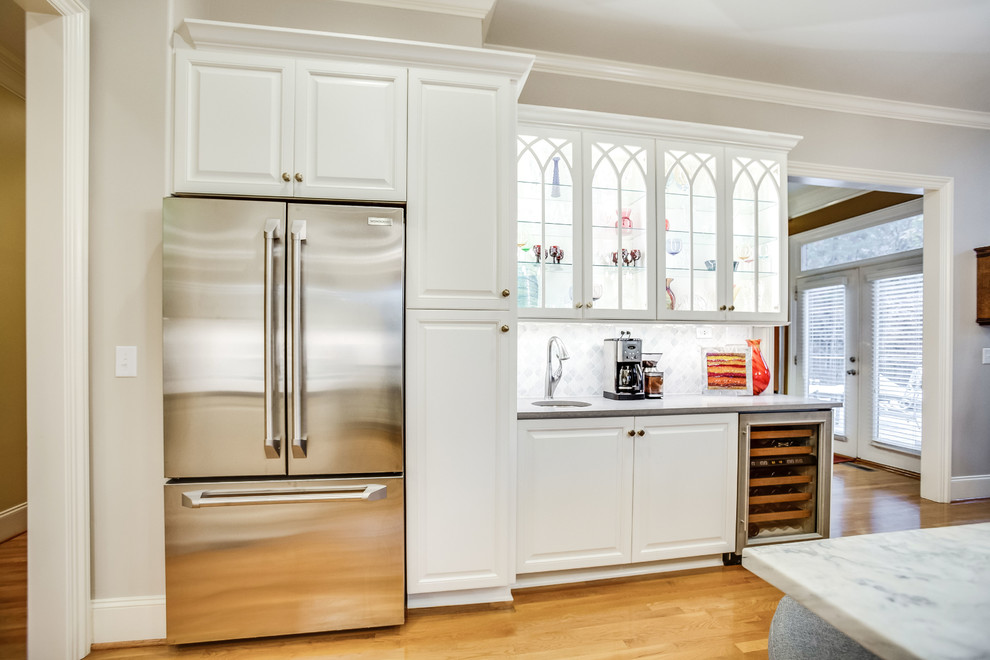 Example of a large transitional u-shaped light wood floor and yellow floor open concept kitchen design in Birmingham with raised-panel cabinets, white cabinets, marble countertops, white backsplash, marble backsplash, stainless steel appliances, an island and white countertops