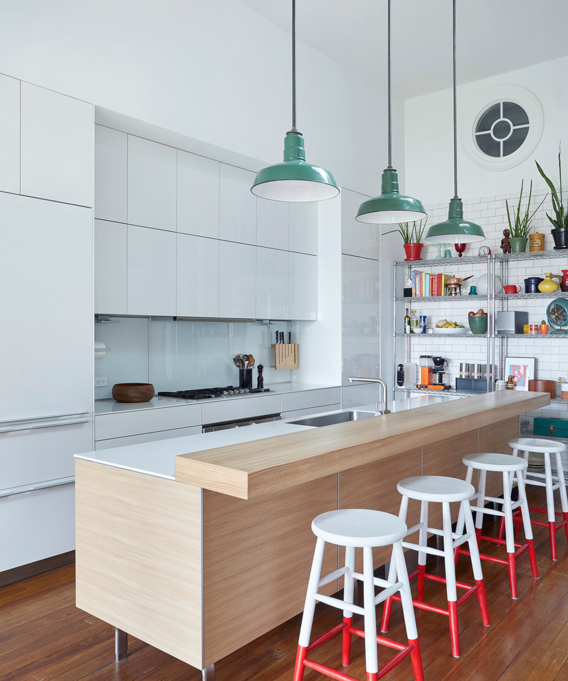 Design ideas for an eclectic galley kitchen in New York with an island, a single-bowl sink, flat-panel cabinets, white cabinets, white splashback, glass sheet splashback, stainless steel appliances, dark hardwood flooring and brown floors.