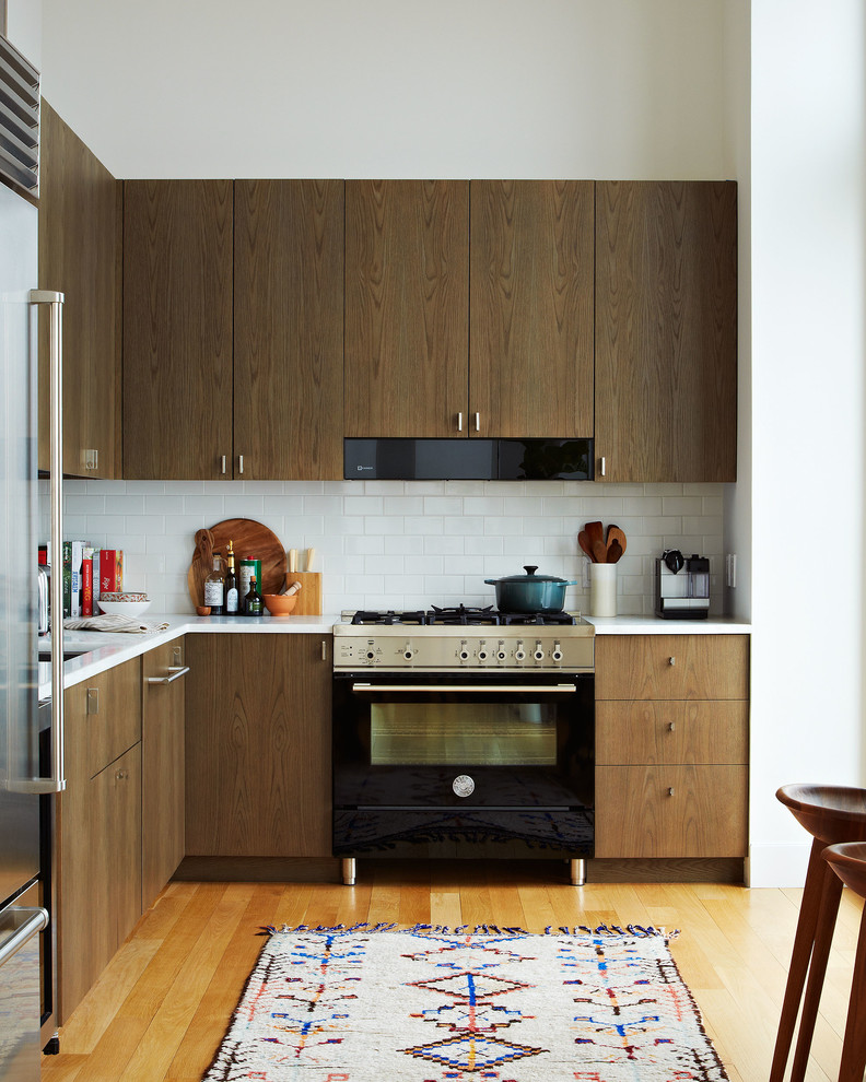 Idée de décoration pour une cuisine nordique en L et bois foncé avec un évier encastré, un placard à porte plane, une crédence blanche, une crédence en carrelage métro, un électroménager noir et un sol en bois brun.