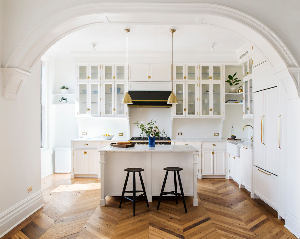Klassische Küche in L-Form mit Landhausspüle, Glasfronten, weißen Schränken, Küchenrückwand in Weiß, schwarzen Elektrogeräten, braunem Holzboden, Kücheninsel und Rückwand aus Metrofliesen in New York