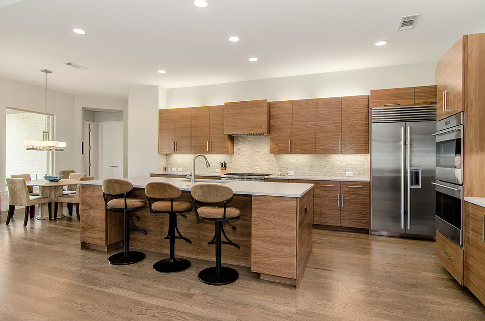 Moderne Wohnküche in L-Form mit flächenbündigen Schrankfronten, hellbraunen Holzschränken, Küchenrückwand in Beige, Küchengeräten aus Edelstahl, braunem Holzboden und Kücheninsel in Dallas