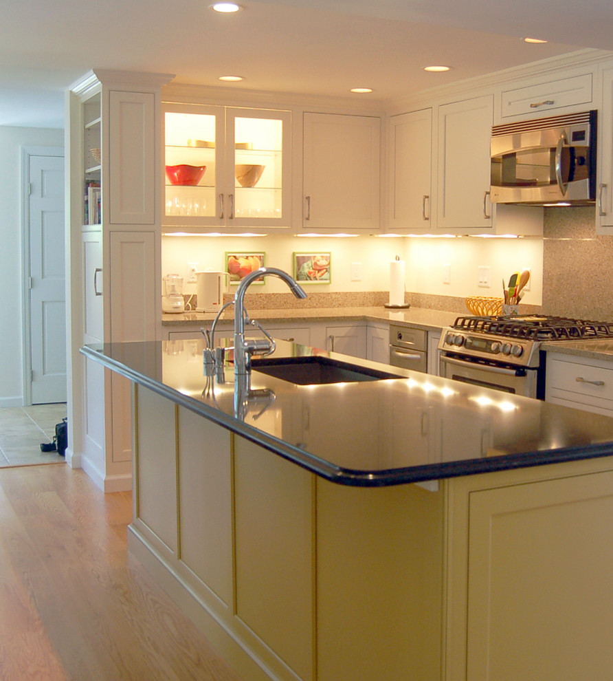 Klassisk inredning av ett mellanstort kök, med en undermonterad diskho, luckor med profilerade fronter, vita skåp, bänkskiva i kvarts, rostfria vitvaror, mellanmörkt trägolv och en köksö
