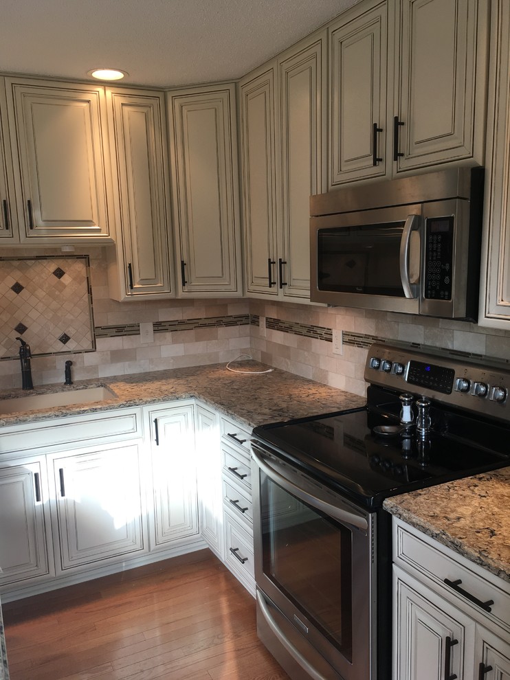 Mid-sized elegant l-shaped medium tone wood floor and orange floor eat-in kitchen photo in New York with an undermount sink, raised-panel cabinets, white cabinets, quartz countertops, beige backsplash, mosaic tile backsplash, stainless steel appliances, an island and brown countertops