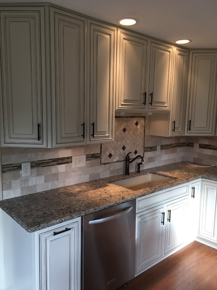 Mid-sized elegant l-shaped medium tone wood floor and orange floor eat-in kitchen photo in New York with an undermount sink, raised-panel cabinets, white cabinets, quartz countertops, beige backsplash, mosaic tile backsplash, stainless steel appliances, an island and brown countertops