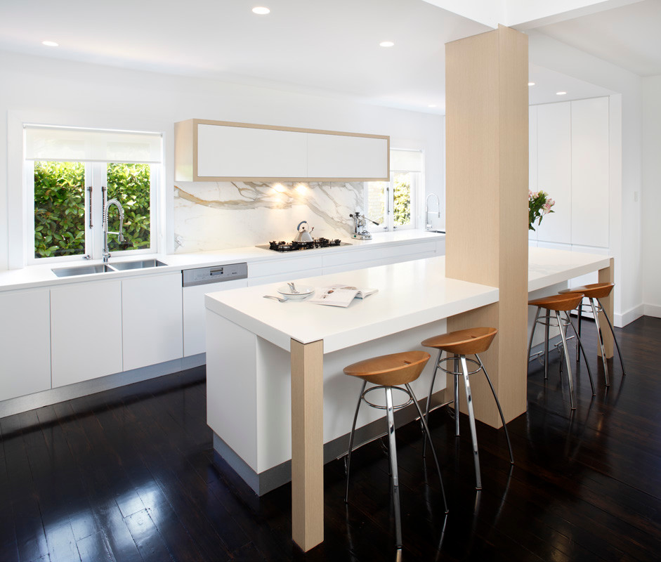 Minimalist single-wall eat-in kitchen photo in Sydney with a drop-in sink, flat-panel cabinets, white cabinets, solid surface countertops, stone slab backsplash and stainless steel appliances