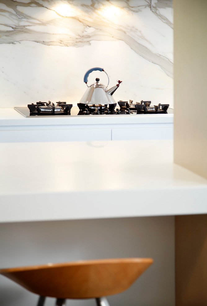 Immagine di una cucina moderna con lavello da incasso, ante lisce, ante bianche, top in superficie solida, paraspruzzi in lastra di pietra e elettrodomestici in acciaio inossidabile