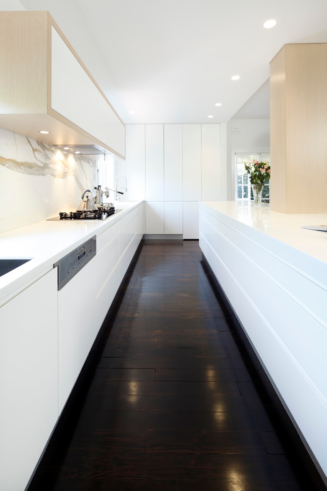 Modelo de cocina lineal minimalista con puertas de armario blancas, encimera de acrílico, salpicadero de losas de piedra, electrodomésticos de acero inoxidable y fregadero bajoencimera