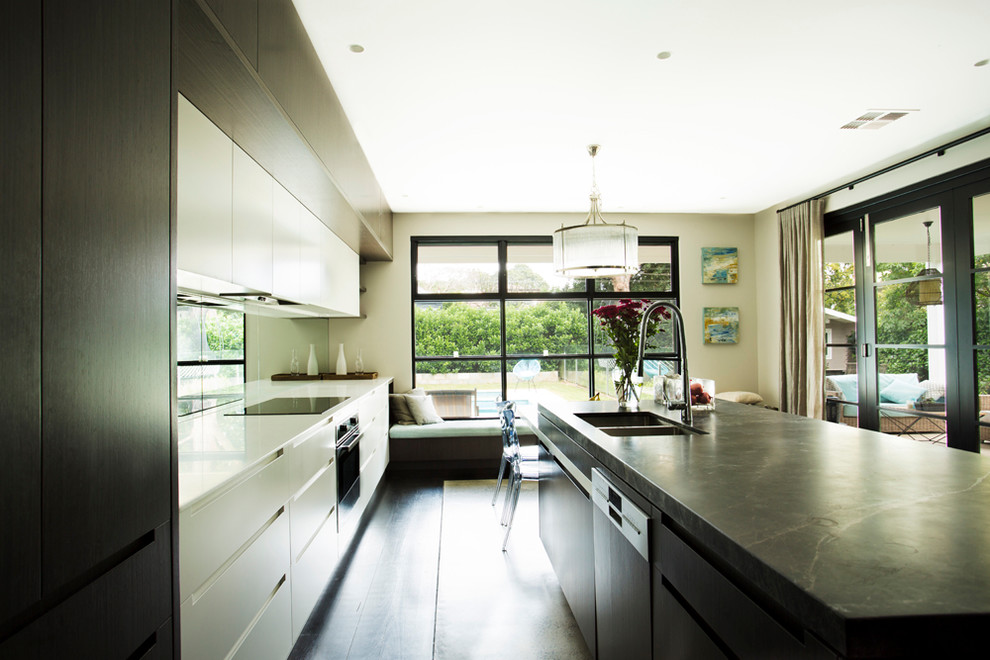 シドニーにあるコンテンポラリースタイルのおしゃれなアイランドキッチン (ダブルシンク、濃色木目調キャビネット、大理石カウンター、ガラス板のキッチンパネル、シルバーの調理設備、コンクリートの床) の写真