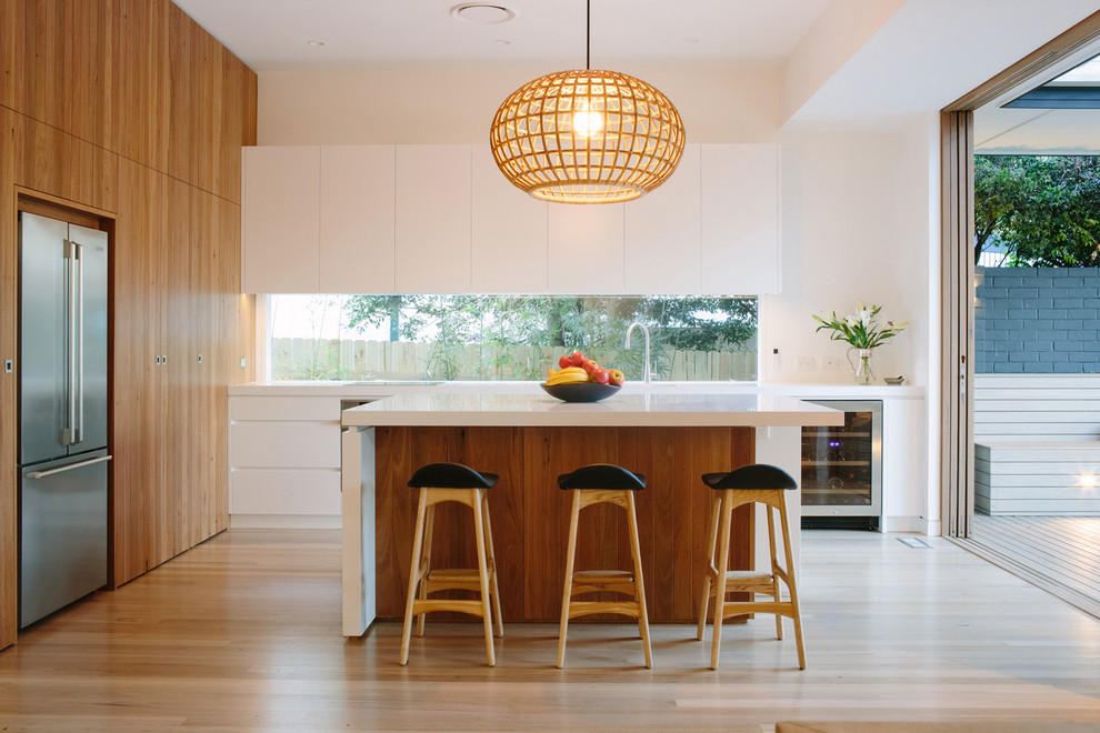 Moderne Küche in L-Form mit flächenbündigen Schrankfronten, weißen Schränken, Küchengeräten aus Edelstahl, hellem Holzboden und Kücheninsel in Sydney