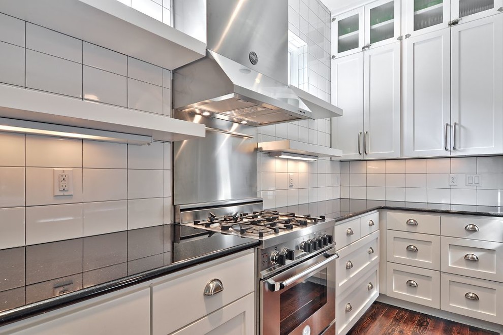 Klassisk inredning av ett kök, med luckor med infälld panel, vita skåp, granitbänkskiva, vitt stänkskydd och stänkskydd i metallkakel