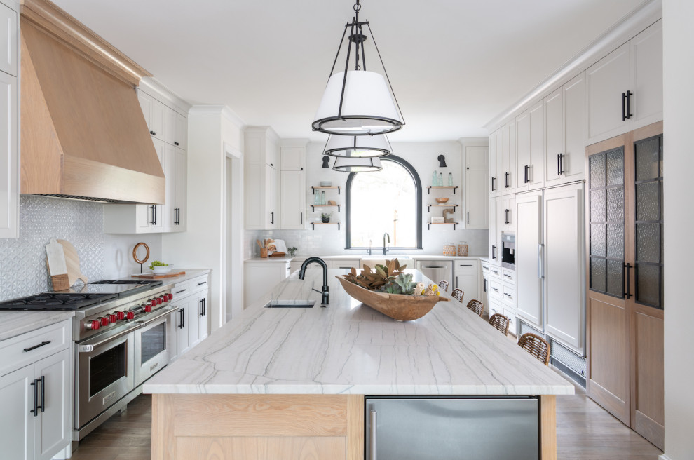 Foto på ett stort nordiskt vit kök, med en undermonterad diskho, luckor med profilerade fronter, skåp i ljust trä, marmorbänkskiva, vitt stänkskydd, stänkskydd i keramik, rostfria vitvaror, ljust trägolv, en köksö och vitt golv