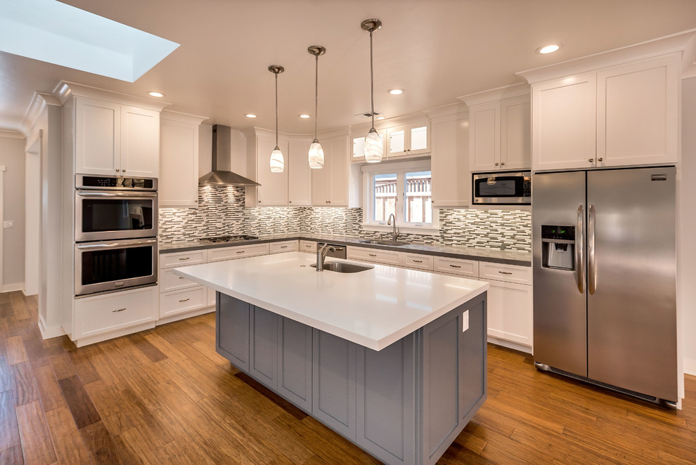 Mid-sized arts and crafts l-shaped medium tone wood floor open concept kitchen photo in San Francisco with an undermount sink, shaker cabinets, white cabinets, quartz countertops, multicolored backsplash, glass tile backsplash, stainless steel appliances and an island