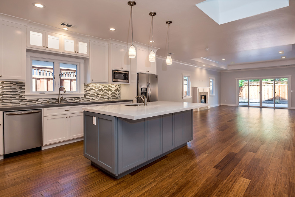 Example of a mid-sized arts and crafts l-shaped medium tone wood floor open concept kitchen design in San Francisco with an undermount sink, shaker cabinets, white cabinets, quartz countertops, multicolored backsplash, glass tile backsplash, stainless steel appliances and an island