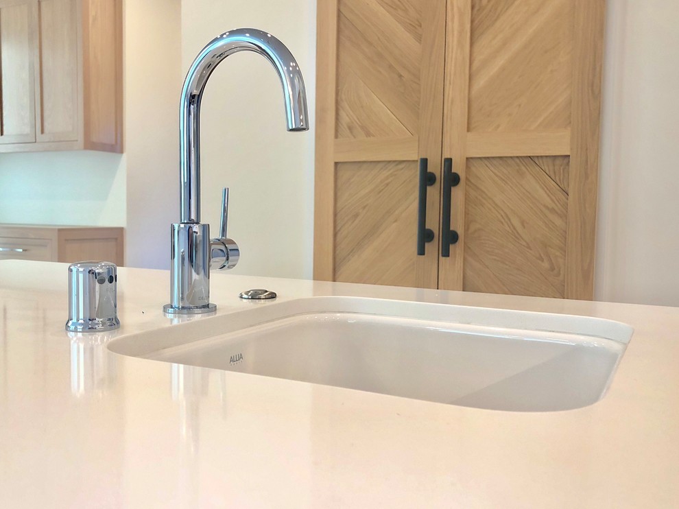 This is an example of a large beach style kitchen in San Francisco with a submerged sink, shaker cabinets, light wood cabinets, quartz worktops, white splashback, porcelain splashback, stainless steel appliances, light hardwood flooring, an island, beige floors and white worktops.