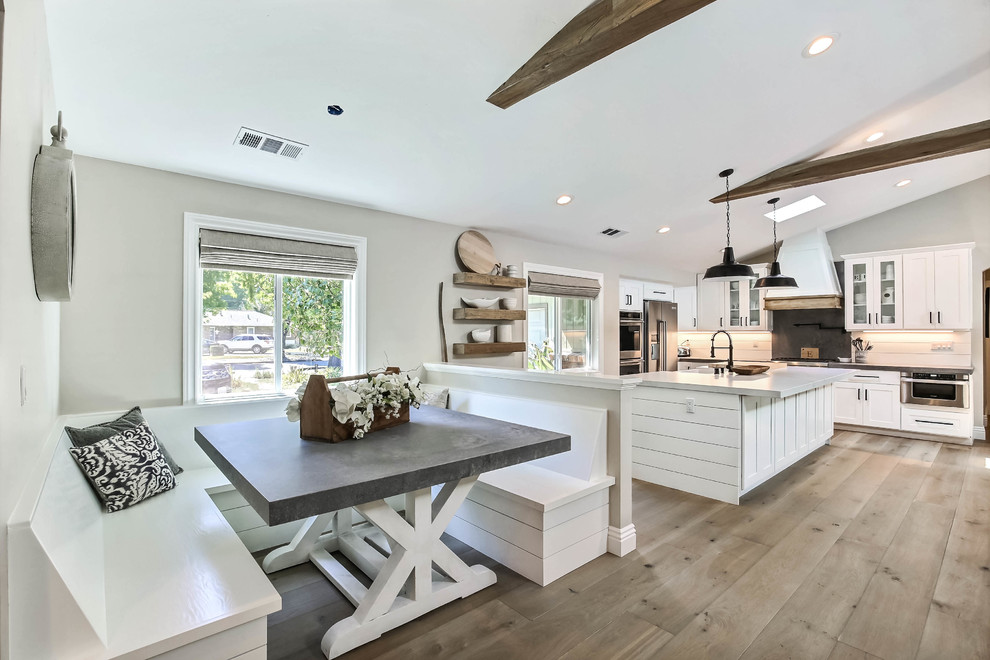 Large farmhouse u-shaped kitchen/diner in San Francisco with a belfast sink, recessed-panel cabinets, white cabinets, engineered stone countertops, cement tile splashback, stainless steel appliances, light hardwood flooring, an island, beige floors and white worktops.