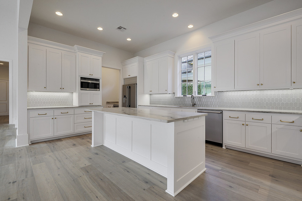 Large classic u-shaped kitchen/diner in New Orleans with a submerged sink, recessed-panel cabinets, white cabinets, engineered stone countertops, grey splashback, ceramic splashback, stainless steel appliances, light hardwood flooring, an island, beige floors and grey worktops.