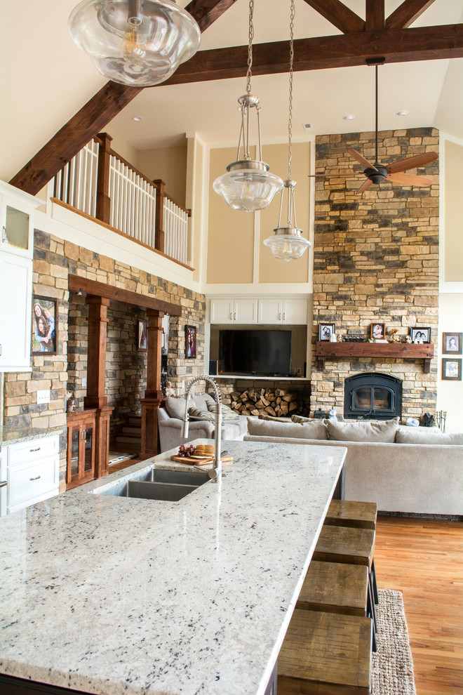 This is an example of a large rustic single-wall open plan kitchen in Charlotte with a double-bowl sink, shaker cabinets, white cabinets, engineered stone countertops, white splashback, stone tiled splashback, stainless steel appliances, light hardwood flooring, an island and white worktops.