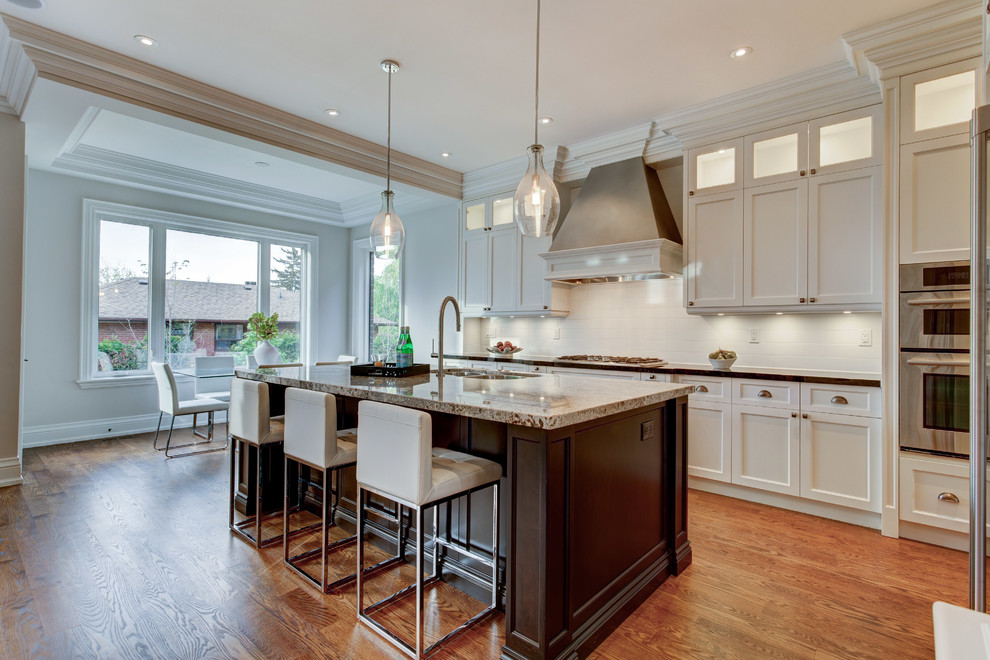 Example of a mid-sized transitional l-shaped dark wood floor open concept kitchen design in Toronto with an undermount sink, shaker cabinets, white cabinets, granite countertops, white backsplash, ceramic backsplash, stainless steel appliances and an island