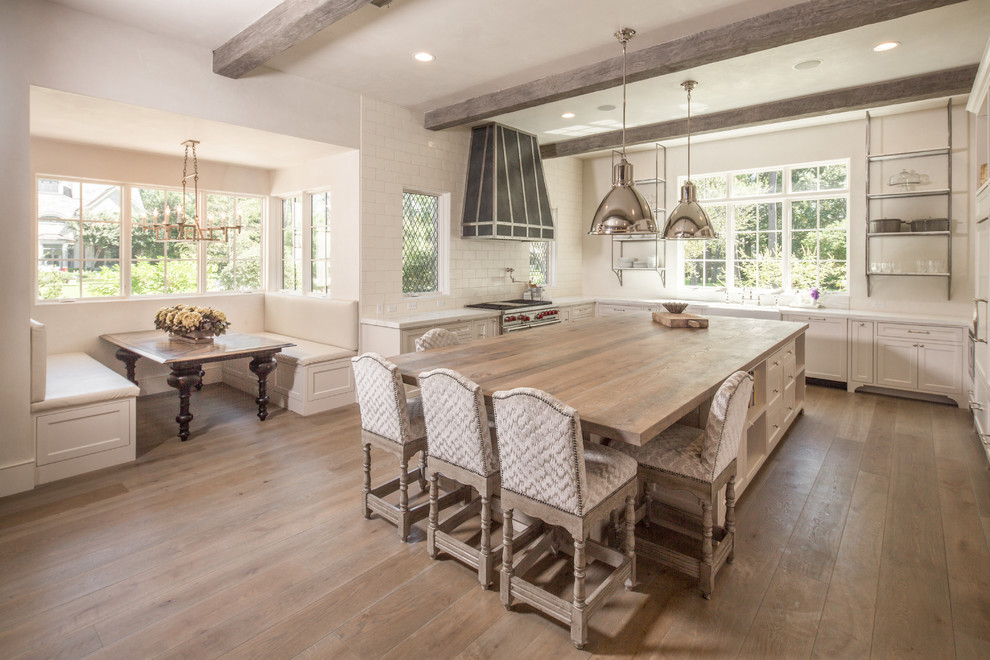 This is an example of a large shabby-chic style u-shaped kitchen/diner in Houston with a belfast sink, shaker cabinets, white cabinets, composite countertops, white splashback, ceramic splashback, stainless steel appliances, medium hardwood flooring, an island and brown floors.