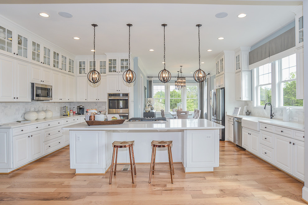 Example of a large transitional l-shaped medium tone wood floor and brown floor open concept kitchen design in DC Metro with an undermount sink, raised-panel cabinets, white cabinets, quartz countertops, white backsplash, stone tile backsplash, stainless steel appliances and an island