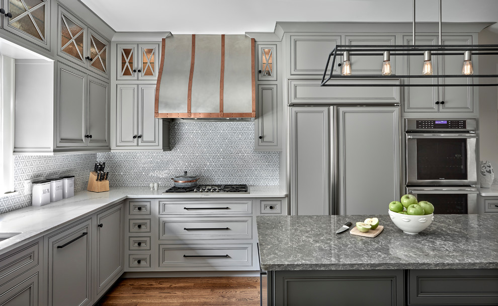 Example of a mid-sized transitional medium tone wood floor and brown floor kitchen design in Chicago with an undermount sink, gray cabinets, solid surface countertops, mosaic tile backsplash, an island, gray countertops, beaded inset cabinets, gray backsplash and paneled appliances