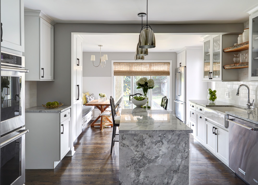 Inspiration for a classic grey and white galley kitchen/diner in Chicago with a belfast sink, white cabinets, quartz worktops, white splashback, stainless steel appliances, an island, shaker cabinets, metro tiled splashback, dark hardwood flooring and brown floors.