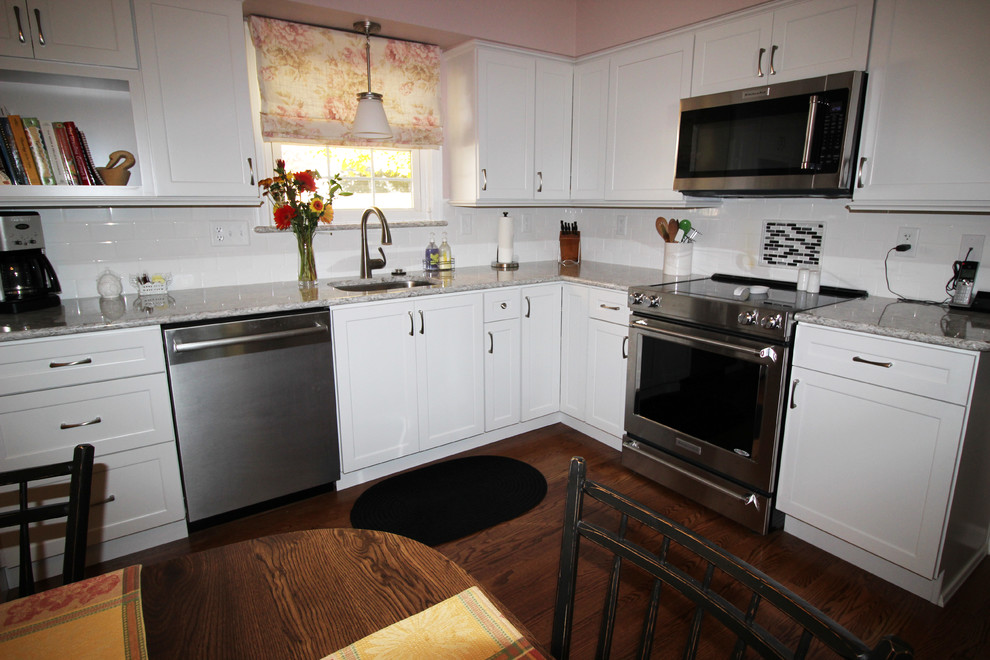 Klassisk inredning av ett mellanstort kök, med vita skåp, bänkskiva i kvarts, vitt stänkskydd, stänkskydd i tunnelbanekakel och rostfria vitvaror