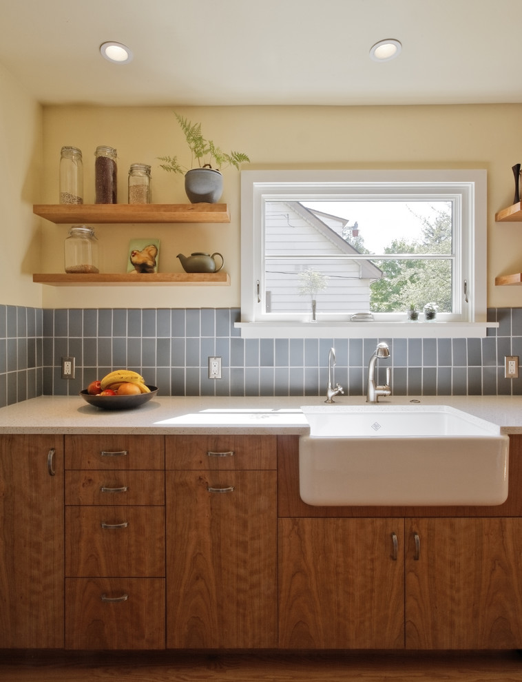 Eat-in kitchen - transitional galley eat-in kitchen idea in Portland with a farmhouse sink, blue backsplash, flat-panel cabinets, medium tone wood cabinets, recycled glass countertops, ceramic backsplash and stainless steel appliances