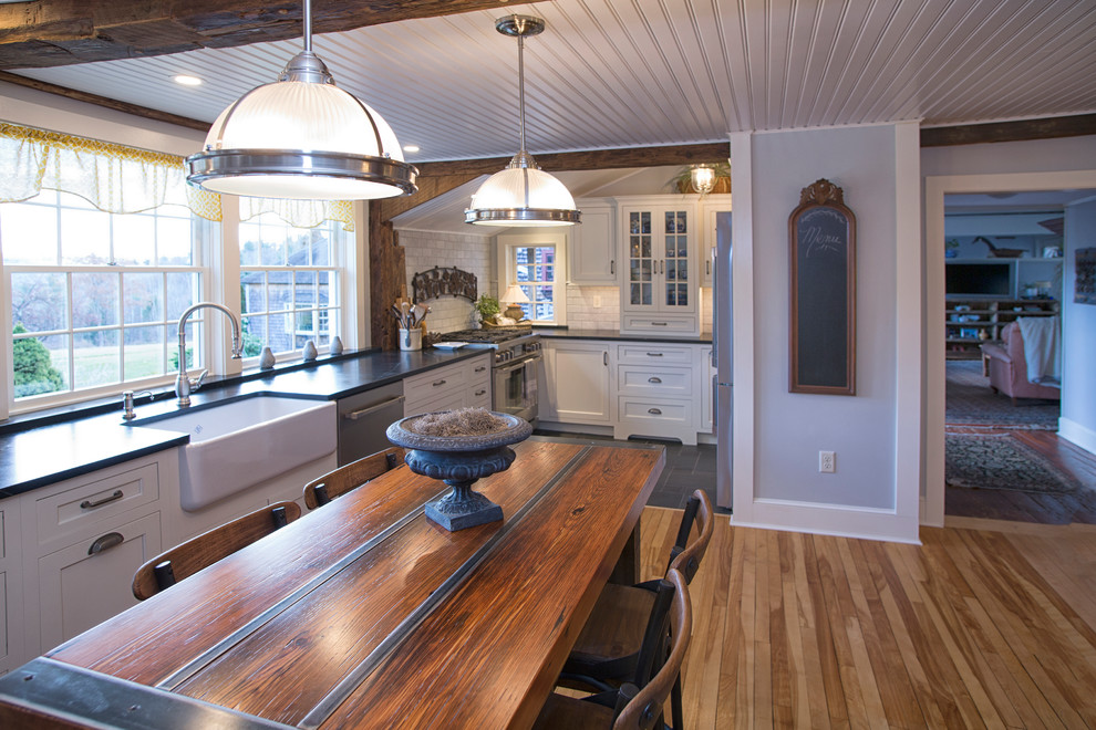 Example of a large country l-shaped light wood floor eat-in kitchen design in Boston with a farmhouse sink, shaker cabinets, white cabinets, soapstone countertops, white backsplash, marble backsplash, stainless steel appliances and an island
