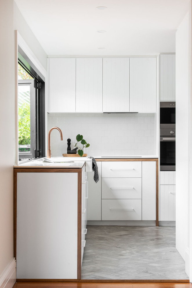 Skandinavische Küche ohne Insel in L-Form mit Landhausspüle, weißen Schränken, Küchenrückwand in Weiß, Rückwand aus Keramikfliesen, Küchengeräten aus Edelstahl und weißer Arbeitsplatte in Hobart