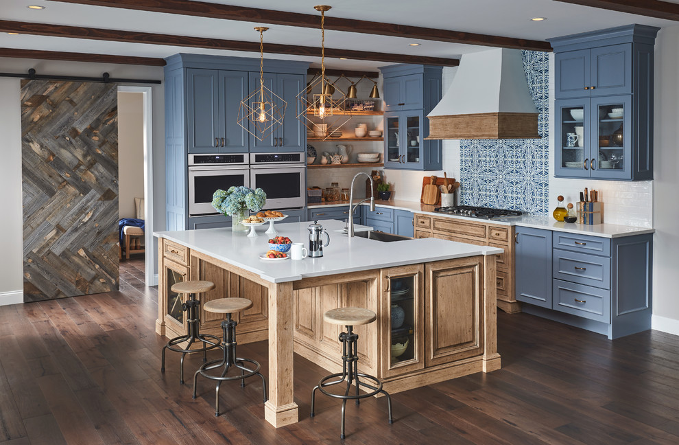 This is an example of a beach style l-shaped kitchen in Austin with a belfast sink, recessed-panel cabinets, blue cabinets, blue splashback, mosaic tiled splashback, dark hardwood flooring, an island, brown floors and white worktops.