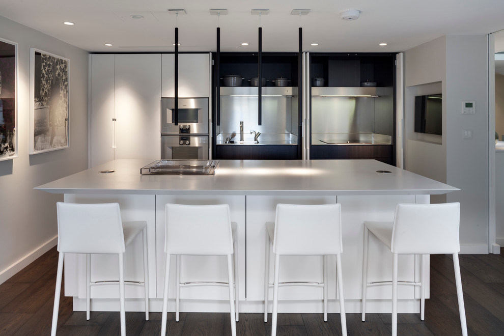 Zweizeilige Moderne Wohnküche mit integriertem Waschbecken, flächenbündigen Schrankfronten, weißen Schränken, Küchenrückwand in Metallic, dunklem Holzboden und Kücheninsel in London