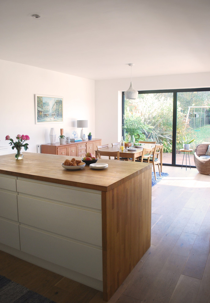 This is an example of a large modern l-shaped kitchen/diner in Wiltshire with a single-bowl sink, flat-panel cabinets, white cabinets, wood worktops, grey splashback, stone tiled splashback, stainless steel appliances, light hardwood flooring and an island.