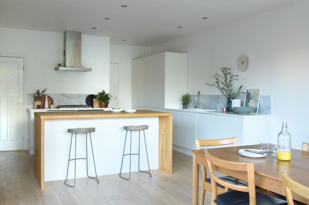Design ideas for a large l-shaped kitchen/diner in Wiltshire with a single-bowl sink, flat-panel cabinets, white cabinets, wood worktops, grey splashback, stone tiled splashback, stainless steel appliances, medium hardwood flooring and an island.