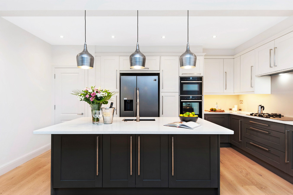 Large transitional l-shaped light wood floor and beige floor kitchen photo in London with shaker cabinets, black cabinets, quartzite countertops, an island, white countertops, an undermount sink and stainless steel appliances