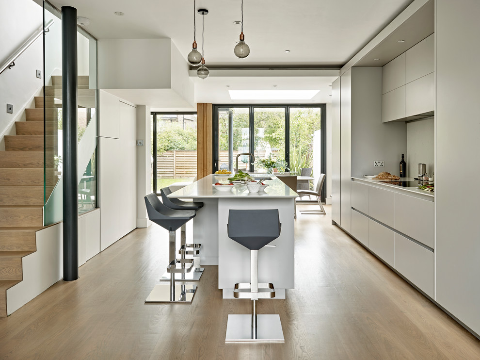 Photo of a medium sized contemporary single-wall kitchen/diner in Surrey with flat-panel cabinets, grey cabinets, an island, a submerged sink, quartz worktops, black appliances, light hardwood flooring and brown floors.
