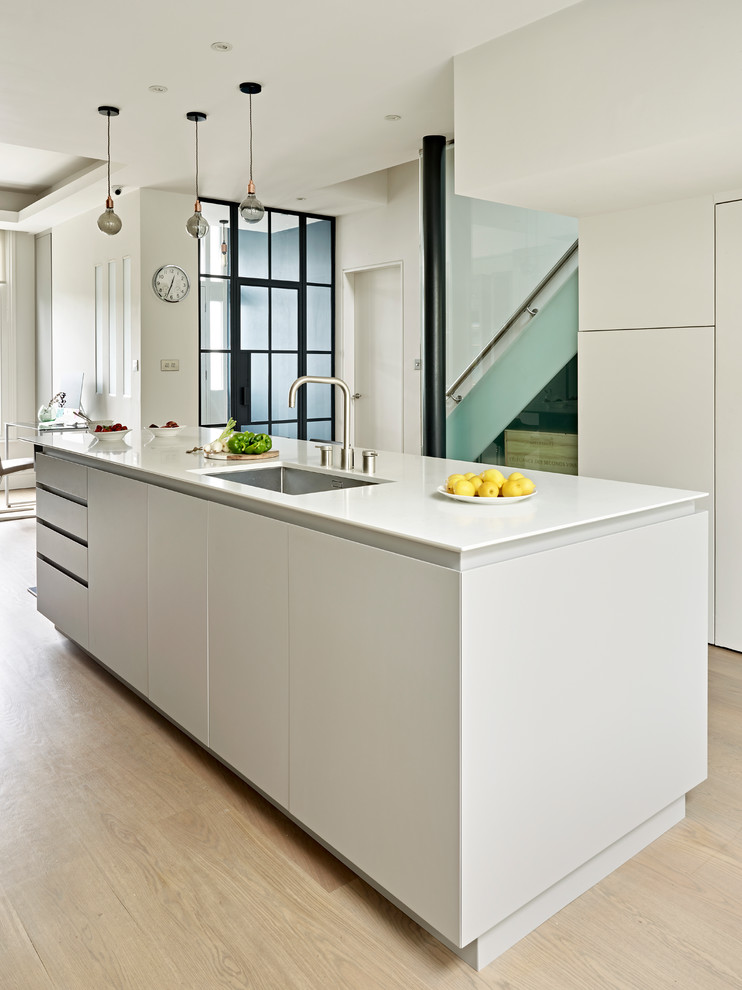 Foto di una cucina minimalista con ante lisce, ante grigie, top in superficie solida, parquet chiaro e pavimento marrone