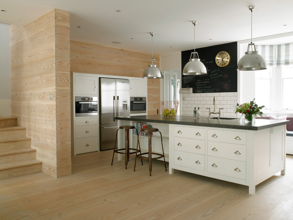 Classic kitchen in London with flat-panel cabinets, white cabinets, white splashback, metro tiled splashback and stainless steel appliances.