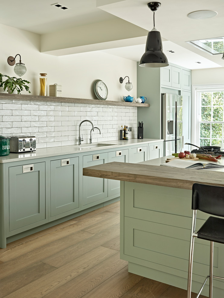 Large traditional single-wall open plan kitchen in London with a built-in sink, shaker cabinets, green cabinets, quartz worktops, white splashback, metro tiled splashback, stainless steel appliances, an island and white worktops.