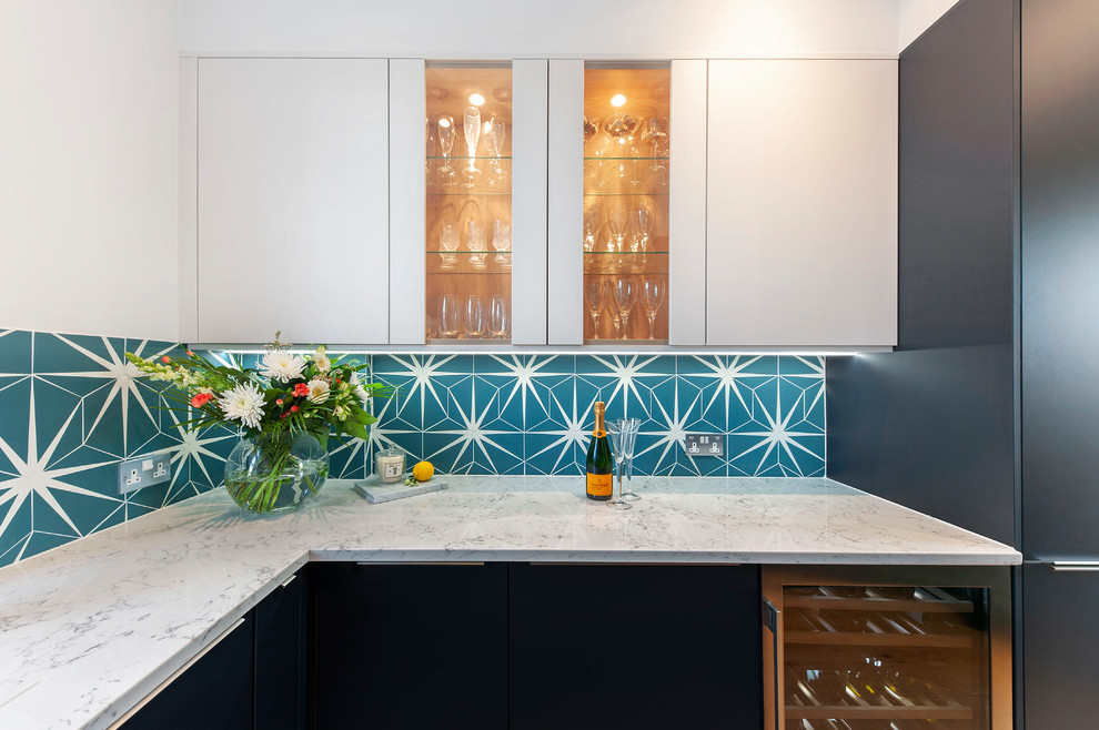 Modern inredning av ett avskilt, litet vit vitt u-kök, med släta luckor, blå skåp, bänkskiva i kvartsit, flerfärgad stänkskydd, stänkskydd i keramik, svarta vitvaror och ljust trägolv