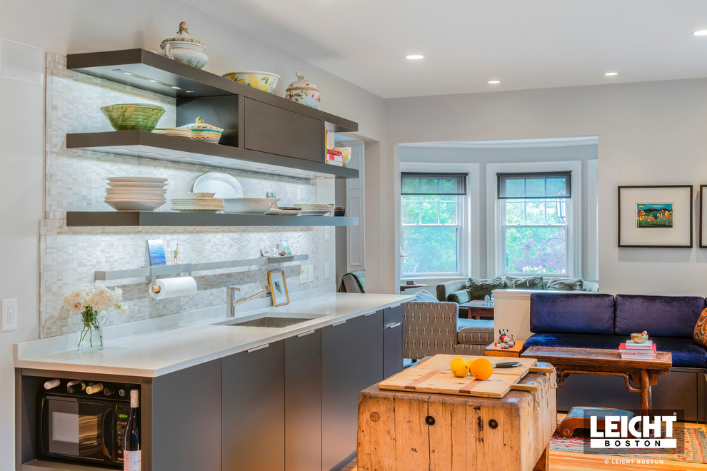 Small trendy galley light wood floor and multicolored floor open concept kitchen photo in Boston with an undermount sink, flat-panel cabinets, gray cabinets, solid surface countertops, multicolored backsplash, stone tile backsplash, stainless steel appliances and an island