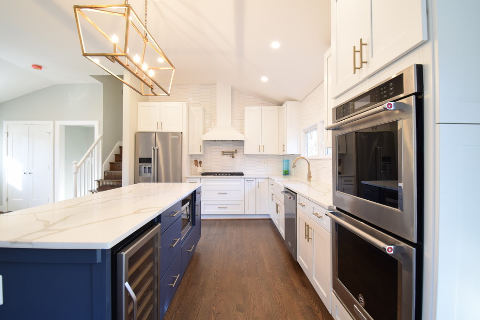 Large transitional l-shaped dark wood floor and brown floor eat-in kitchen photo in Baltimore with a farmhouse sink, shaker cabinets, white cabinets, quartz countertops, white backsplash, cement tile backsplash, stainless steel appliances, an island and white countertops