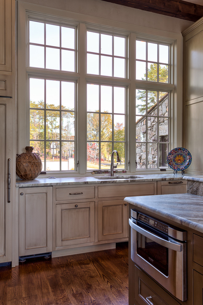 Foto di una cucina classica di medie dimensioni con ante a filo, parquet scuro, ante con finitura invecchiata, top in marmo, elettrodomestici in acciaio inossidabile e lavello sottopiano