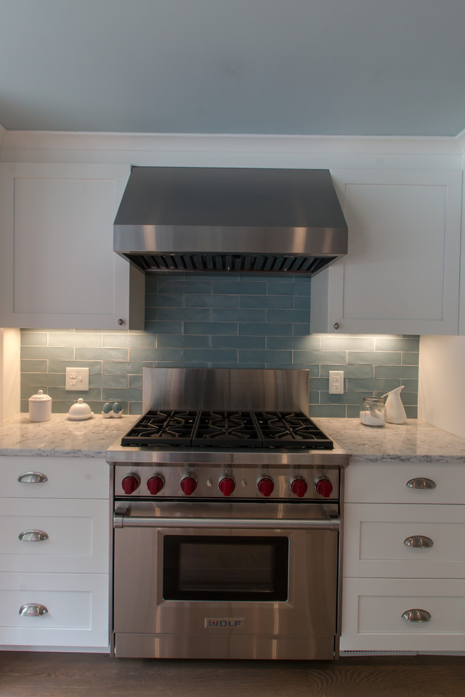 Inspiration for a timeless u-shaped medium tone wood floor kitchen remodel in Boston with a farmhouse sink, recessed-panel cabinets, white cabinets, quartz countertops, blue backsplash, glass tile backsplash, stainless steel appliances and an island
