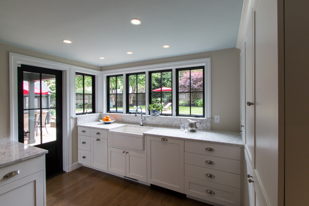 Inspiration for a timeless u-shaped medium tone wood floor kitchen remodel in Boston with a farmhouse sink, recessed-panel cabinets, white cabinets, quartz countertops, blue backsplash, glass tile backsplash, stainless steel appliances and an island