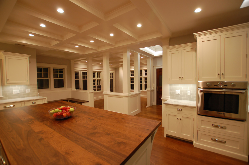 Klassisk inredning av ett stort beige beige kök, med en nedsänkt diskho, luckor med profilerade fronter, vita skåp, bänkskiva i kvartsit, grått stänkskydd, stänkskydd i keramik, rostfria vitvaror, mellanmörkt trägolv och en köksö