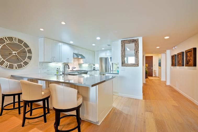 Foto på ett mellanstort maritimt kök, med en undermonterad diskho, skåp i shakerstil, vita skåp, bänkskiva i kvarts, grått stänkskydd, stänkskydd i stenkakel, rostfria vitvaror, ljust trägolv och en halv köksö