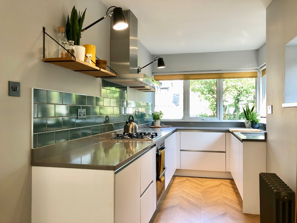 Inredning av ett modernt mellanstort grå grått kök, med en integrerad diskho, släta luckor, vita skåp, bänkskiva i kvarts, grönt stänkskydd, stänkskydd i keramik, rostfria vitvaror, laminatgolv och beiget golv