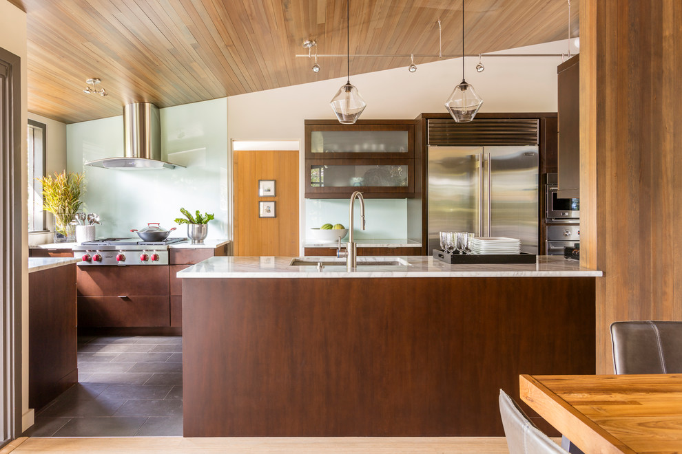 Rustic kitchen/diner in Seattle with a submerged sink, glass-front cabinets, dark wood cabinets, glass sheet splashback, stainless steel appliances, a breakfast bar and brown floors.