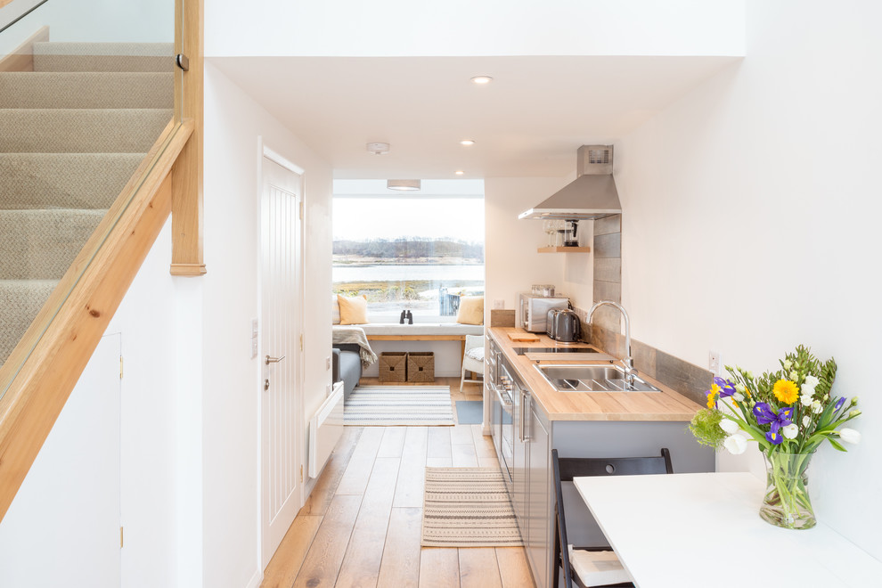 Photo of a small coastal galley open plan kitchen in Other with a single-bowl sink, shaker cabinets, grey cabinets, wood worktops, metallic splashback, integrated appliances, medium hardwood flooring, no island and brown worktops.
